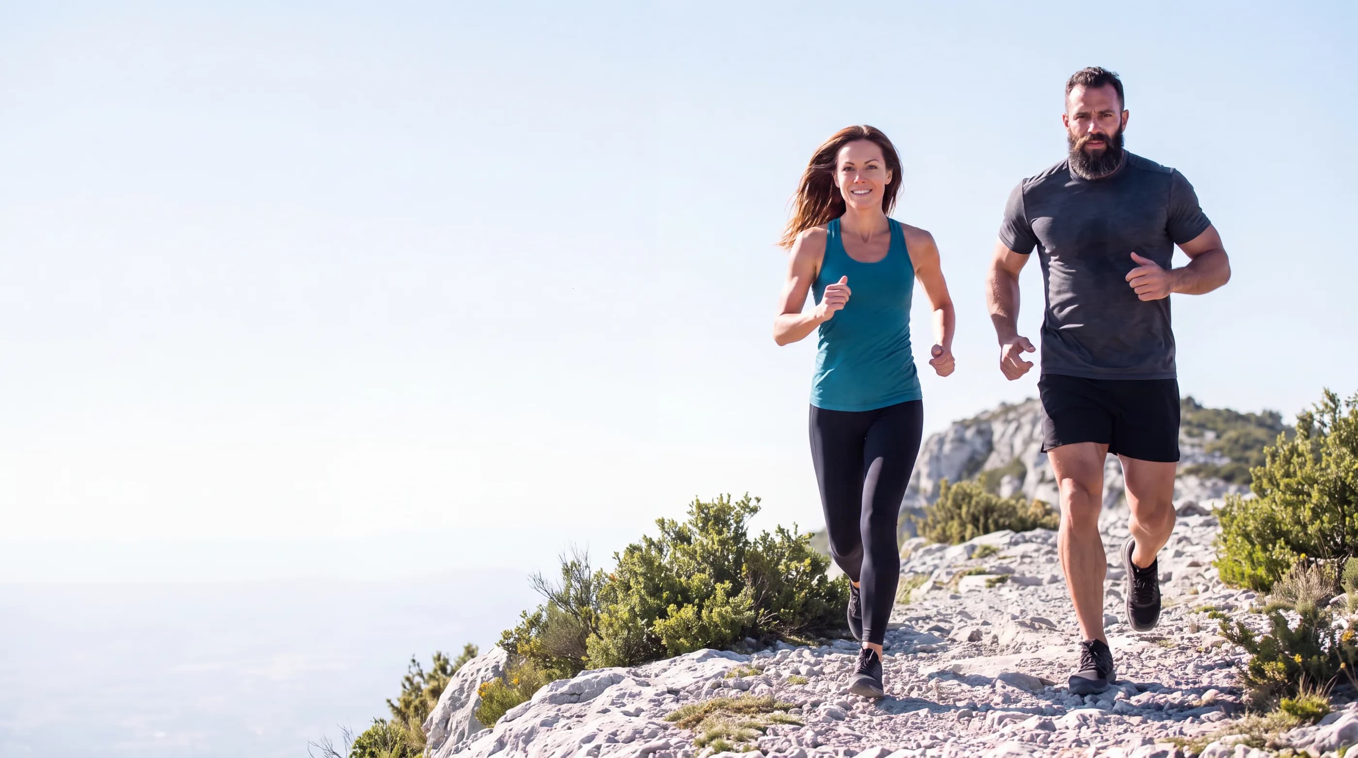 A man and a woman running together on a coastal ridge trail in bright morning light